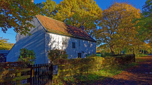 Whitewashed cottage surrounded by trees with leaves turning from green to orange in autumnof